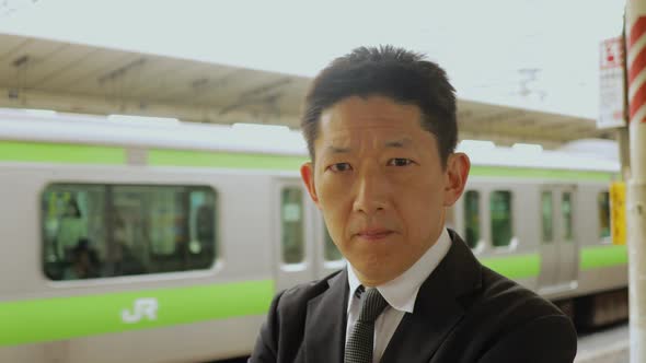 Japanese businessman waiting on a train platform alt