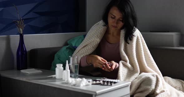 Sick woman putting medicine in hand and take it, drinking water while recovering at home alt