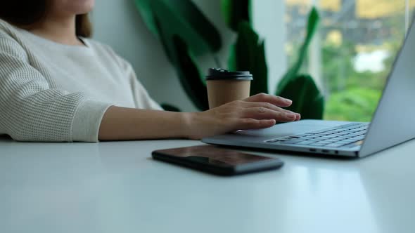 a woman drinking coffee while working and touching on laptop computer touchpad