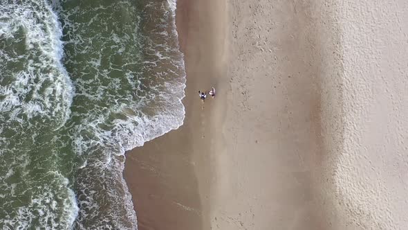 AERIAL: Top View of Young Couple Walking Near Sea Shore on Cloudy Day alt