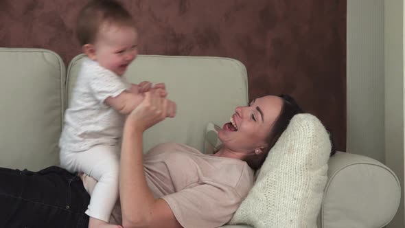Happy Mother Holding Little Baby By Hand and Kissing on Sofa