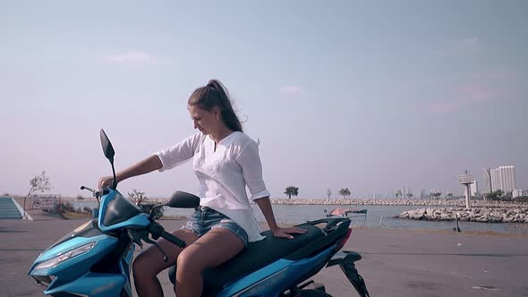Young Woman with Long Hair Sits on Black and Blue Scooter alt