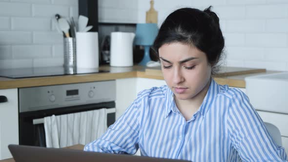 A serious Young Indian girl in a blue striped shirt is working on a computer at home  alt