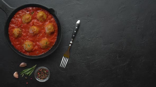 Cooking meatballs with tomato sauce in black pan