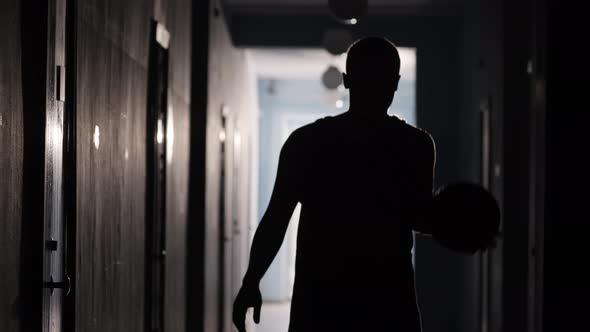 Silhouette of Athlete Walking in Hallway and Dribbling the Basketball