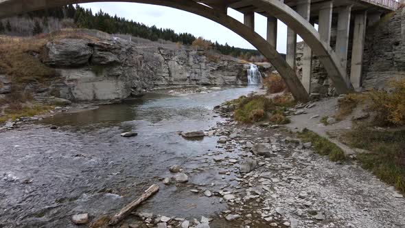 Slo-Mo aerial shot approaching Lundbreck falls while flying underneath an arch bridge in southern Al alt