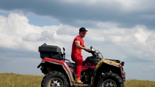 Man in a Black Cap and Red T-shirt on a Colored ATV Rides alt