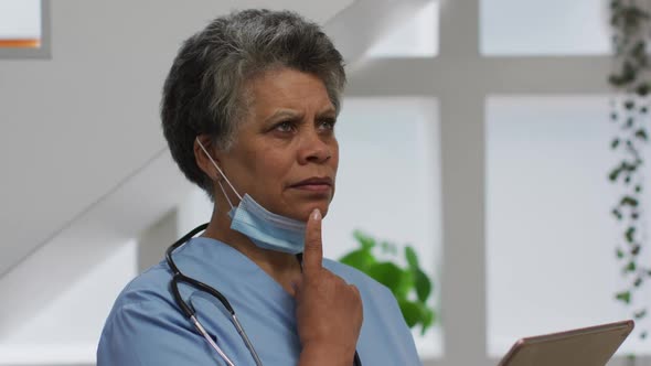 Senior african american female doctor wearing face mask using digital tablet alt