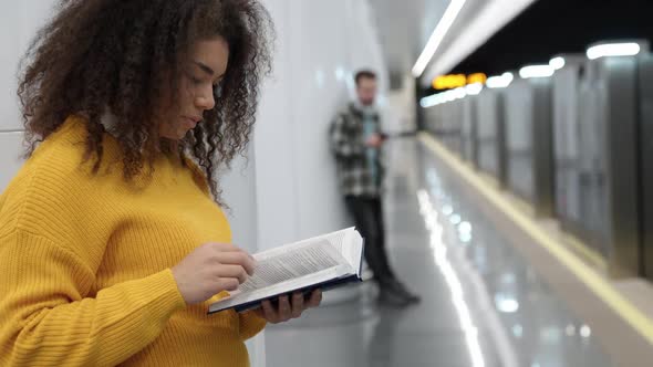African Female Waits for a Train in the Subway and Reads a Book a Young Students Goes to Study at alt