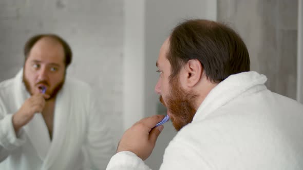 Young Man with Toothbrush Cleaning Teeth and Looking Mirror in Bathroom alt