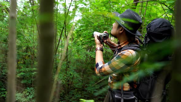 man traveler with backpack using camera to take a photo in the natural forest alt