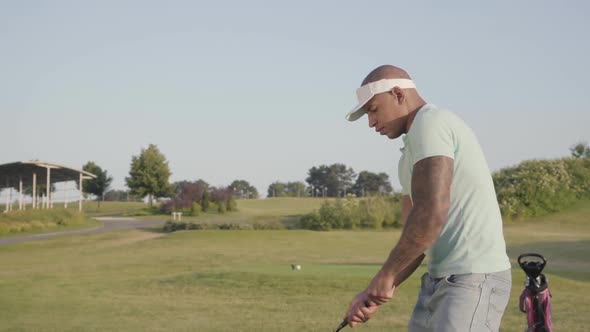 Young Concentrated Middle Eastern Man with Tattoo on the Shoulder Playing Golf on the Golf Field alt