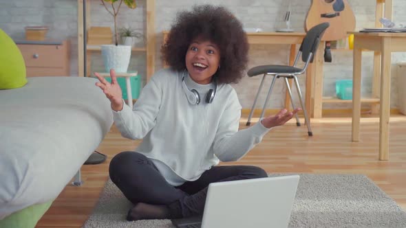 Beautiful African American Woman with an Afro Hairstyle Sitting on the Floor with a Laptop Learned alt