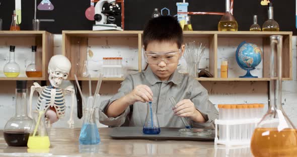 Laboratory Experience in a Chemistry Lesson, Asian Boy in Protective Glasses Pours a Blue Liquid alt
