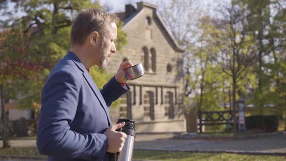 A Middleaged Caucasian Man Drinks Tea From a Vacuum Bottle in a Rural Area in Fall