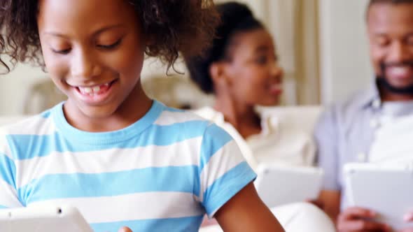 Parents and daughter using digital tablet in living room alt