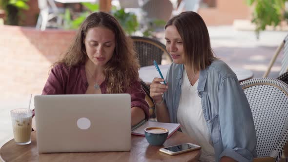 Happy Female Friends Working Together with Laptop at Outdoor Cafe alt