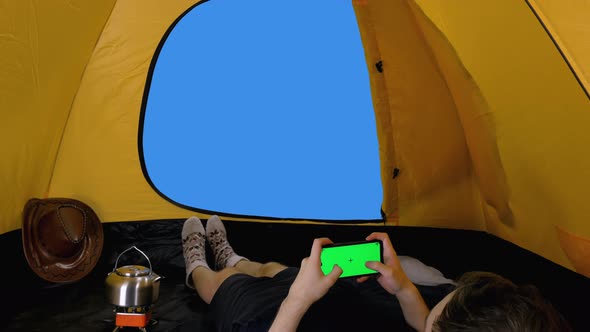 Camper Lying in Open Tent and Using Smartphone with Green Screen while a Man Passing By