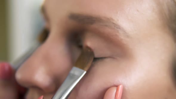 The Makeup Artist Puts Light Shiny Eyeshadow on a Model's Eyelids Using Two Professional Brushes alt