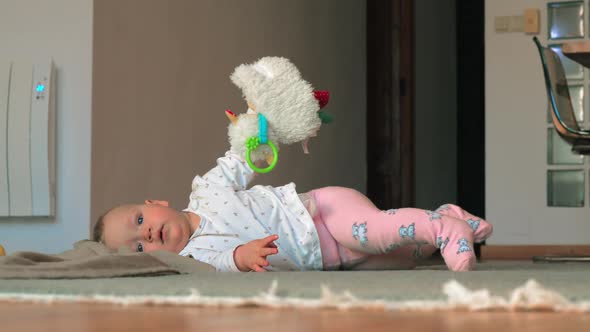 A Baby Girl in Pink Tights Lying on a Floor with Toy Sheep alt