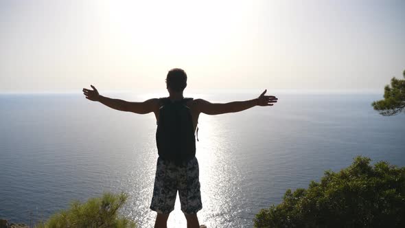 Male Hiker Standing on Peak and Victoriously Raising Hands Rejoicing Achievement or Success