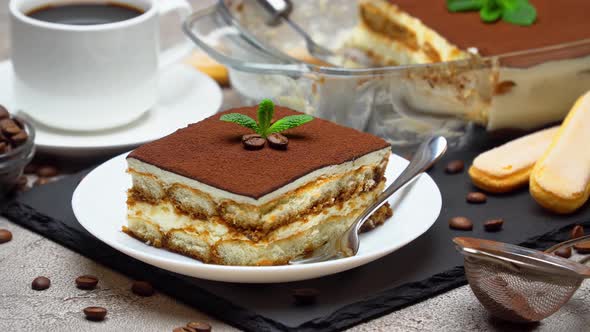 Traditional Italian Tiramisu dessert in glass baking dish and portion on grey concrete background alt