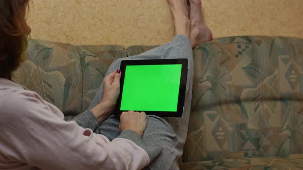 An Adult Woman Lies on a Sofa and Looks at a Tablet