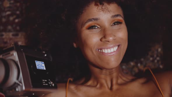 Woman With Afro Hair Smiling With Vintage 8Mm Camera alt