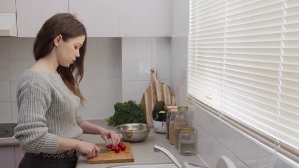 Young female cutting tomatoes in the kitchen. Chopping vegetables for salad