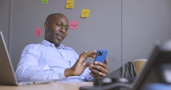 Smiling businessman sitting at desk in office, using smartphone
