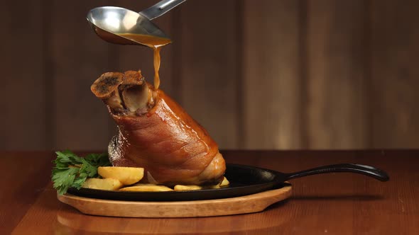 Pour the Pork Knuckle with the Sauce From the Ladle. Ready Meat Dish with Garnish in a Frying Pan