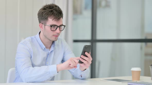 Young Man Celebrating Success on Smartphone in Office alt