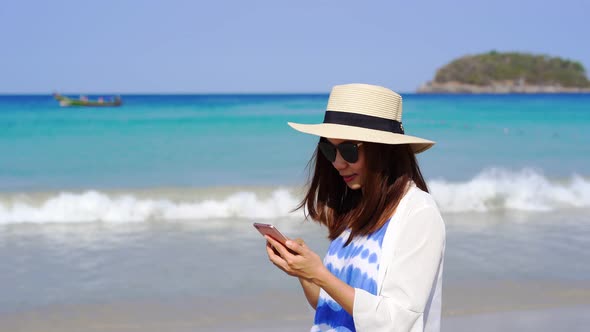 Young asian woman traveler using her smartphone at tropical sand beach