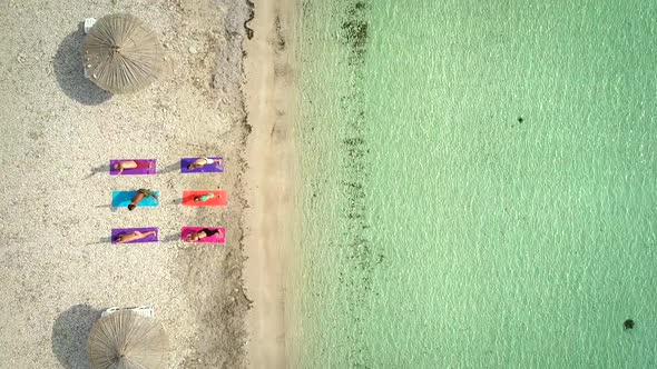 Aerial view of group of people in yoga pose on colourful mats on the beach. alt
