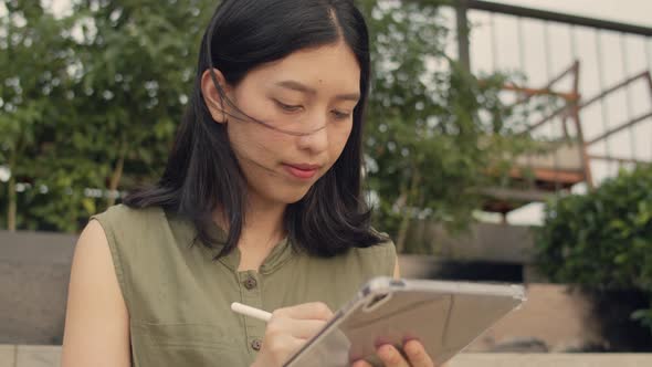 Asian female using tablet working while sitting on a rooftop at sunset.