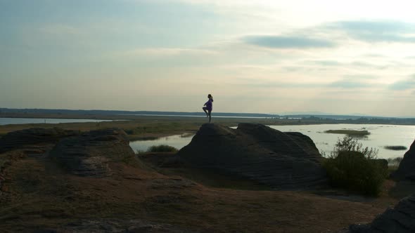 A Girl is Doing Fitness on a Hill on the Lake Shore