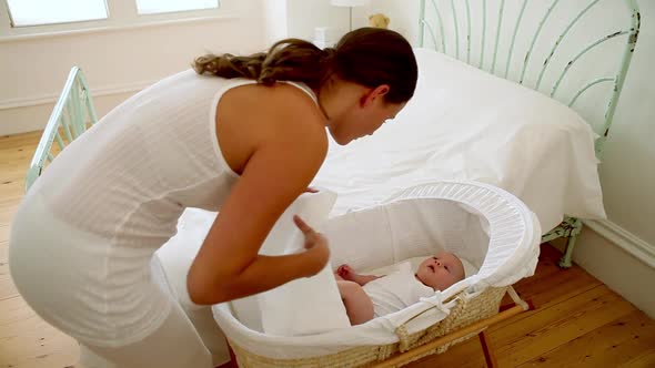 Tired mother putting baby in bassinet and lying on bed alt