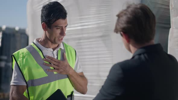 Portrait of Warehouse Manager in Uniform Persuading Convincing Supervisor in Suit Pointing at Packed alt