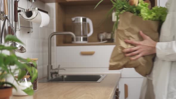 A Young Woman Brings A Paper Bag With Various Products And Puts It On The Kitchen Table alt