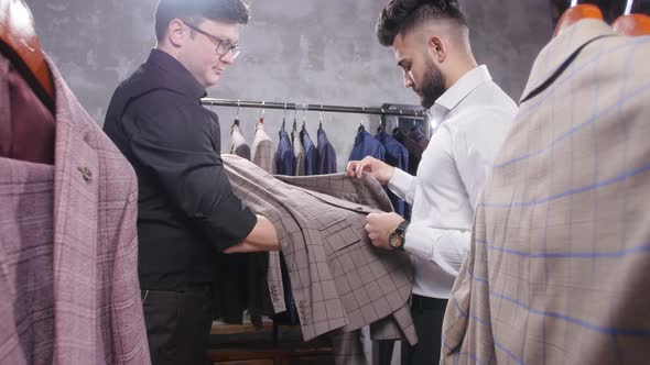 Seller in the Costume Shop Helps the Young Man To Choose a Suit alt