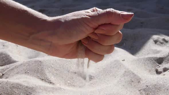 Sand Grains Pour Through Fingers of Female Hand on Beach