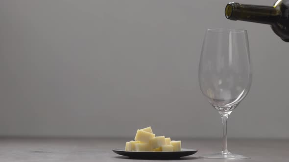 Slow Motion Pour Red Wine Into Wineglass with Hard Cheese on Background on Wood Table alt