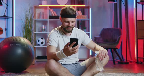 Guy in Sportswear Sitting on the Floor with Crossed Legs, Drinking water alt