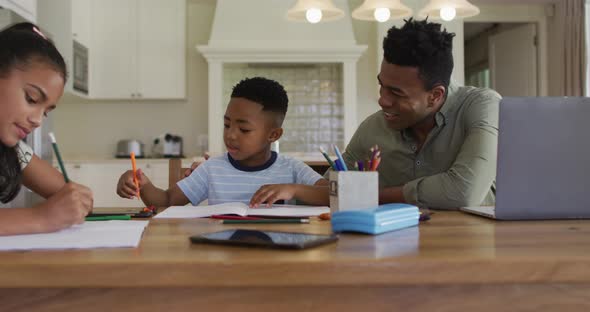African american father, daugher and son sitting at kitchen table doing homework alt