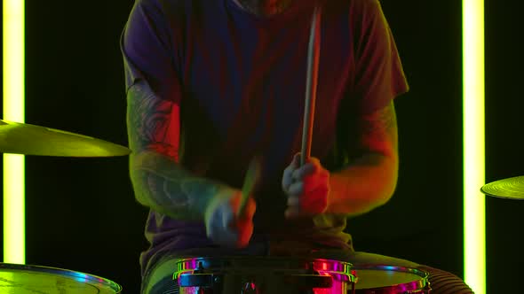 Skilled Man Musician Plays Contemporary Drum Kit in a Dark Studio Illuminated By Multicolored Neon alt