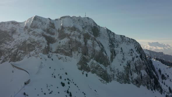 Drone flying towards distant radio tower on top of snow covered mountain summit alt