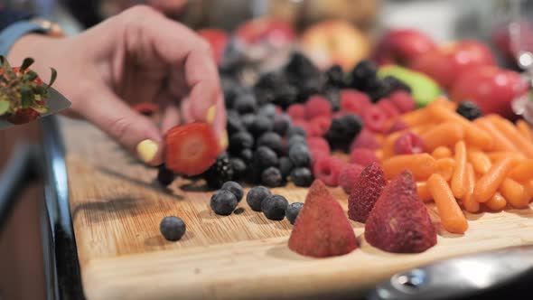 Close up of woman slicing stems off fresh strawberries with kitchen knife. alt