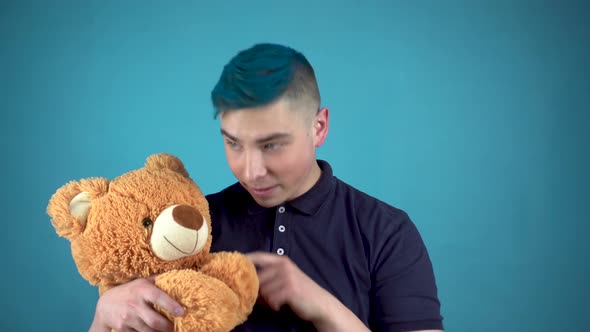 A Young Man with Blue Hair Is Holding a Teddy Bear. Alternative Man Waves His Hand and Looks at the alt