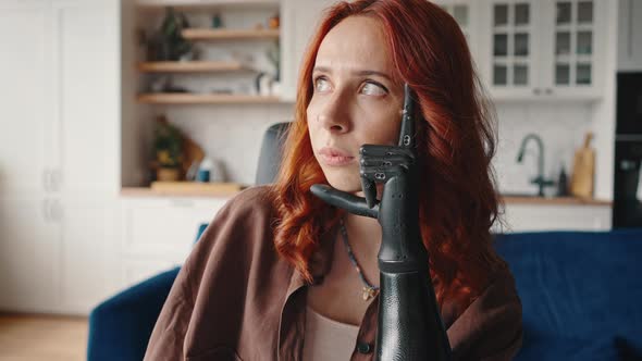 Adult Redhaired Girl with a Modern Hightech Prosthesis Instead of an Amputated Arm Sits in Thought alt