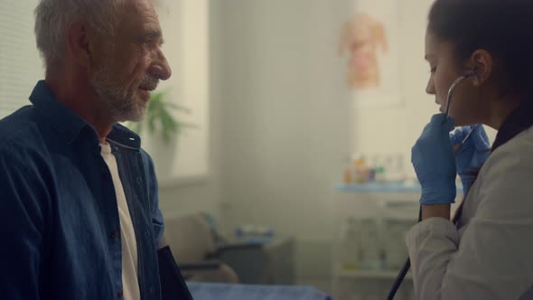 Woman Therapist Checking Pulse Elderly Patient in Clinic Using Stethoscope alt